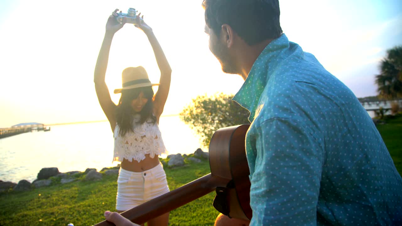 히스패닉 여성이 사진을 찍고 백인 남자가 기타를 연주하고 있습니다.