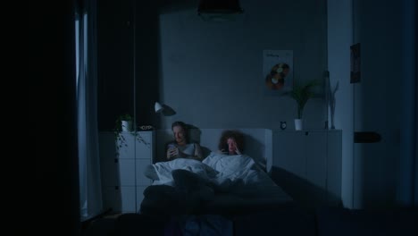 pareja en la cama usando teléfonos por la noche