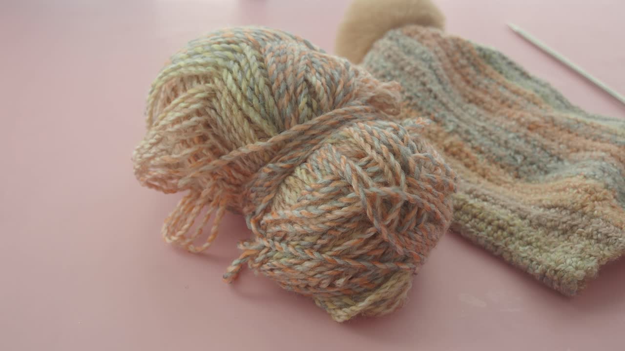 Yarn, knit cap, and knitting needles on a pink surface