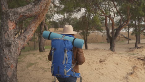 una irreconocible mujer pelirroja aventurera caminando por los árboles de un bosque y al lado de un hermoso lago