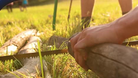 hand saws a log outdoors during summer scout camp, close up slow motion