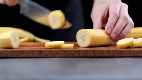 el plátano se corta en pedazos individuales en una tabla de cortar de madera por el cocinero, el tiro de la sartén