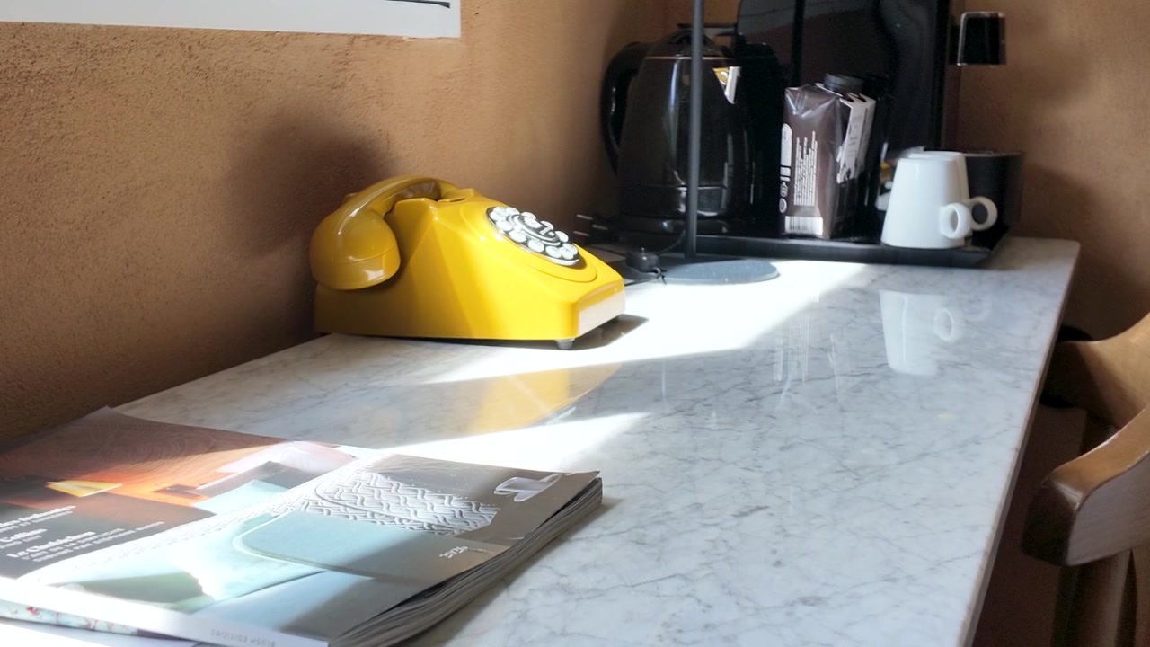A slow zoom focuses on a retro yellow telephone atop a sunlit marble desk