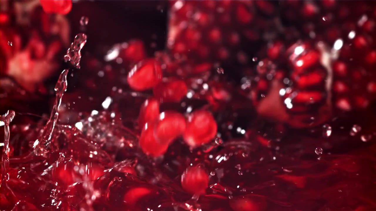 Semi di melograno che cadono e schizzano in un liquido rosso al rallentatore