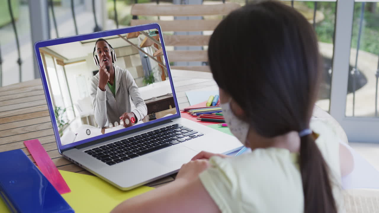 Caucasian girl wearing face mask having a video call on laptop at home