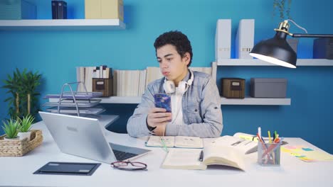 Phone-addicted-teenager-looking-at-the-phone-at-the-table,-looks-his-homework,-hangs-up-and-starts-studying.