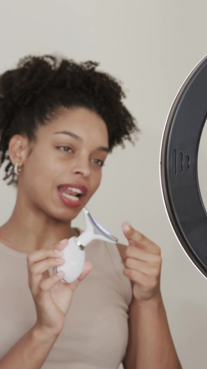 Vertical video: Picking up device, presenter in tan top demoing features at vanity with ring light