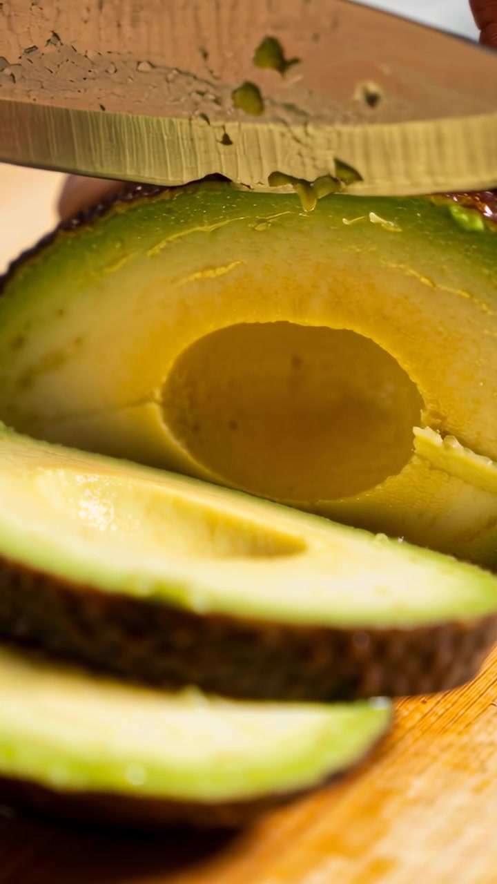 Video verticale: Posizionando il coltello da chef su metà avocado, la mano del cuoco affetta la polpa su un tagliere per preparare un toast.