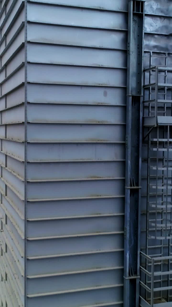 High metal rectangular premise emitting thick grey smoke. Going up along the one of the constructions at modern silo complex. Vertical video