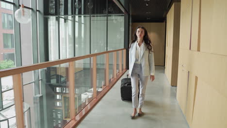 a brunette young businesswoman walks backwards with a trolley. she is on his way to an important business trip.