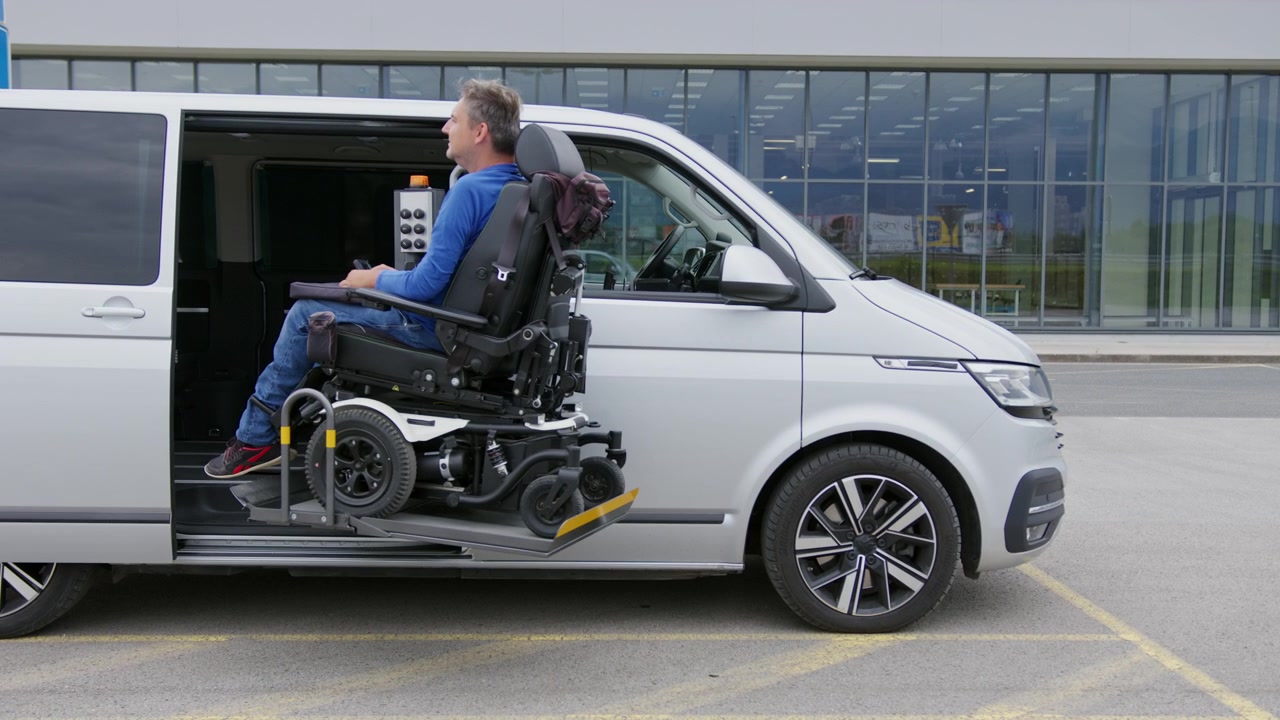 Man in a powered wheelchair using a vehicle wheelchair lift to exit an adapted van independently