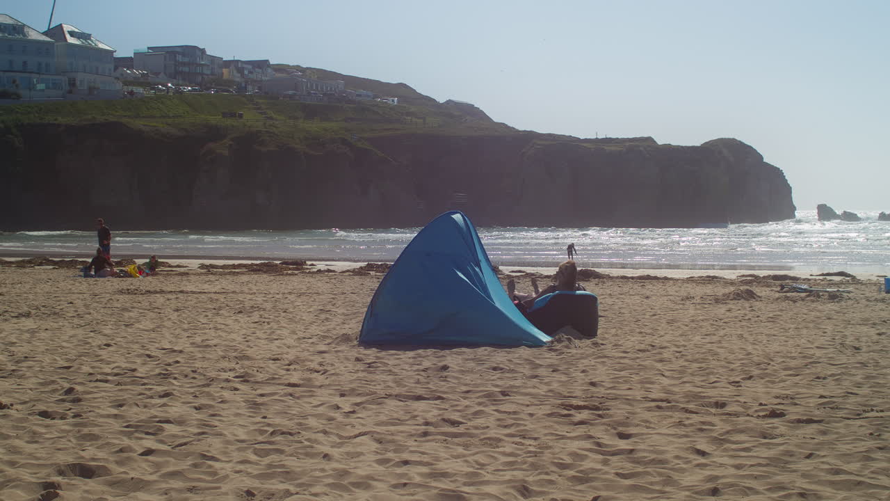 화창한 오후, 콘월, 영국 - 와이드 샷에 perranporth 해변에서 반짝이는 바다의 전망과 함께 휴식을 취하는 관광객