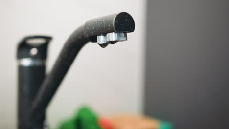 gotas de agua gotean desde el grifo moderno oscuro en el fregadero