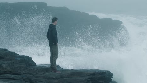 man standing at the cliff with waves crashing in the background