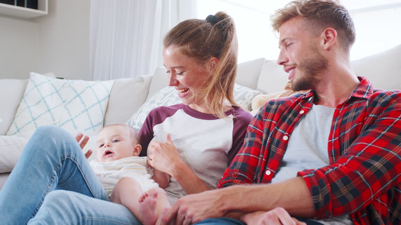 una joven pareja blanca relajándose en la sala de estar con su bebé