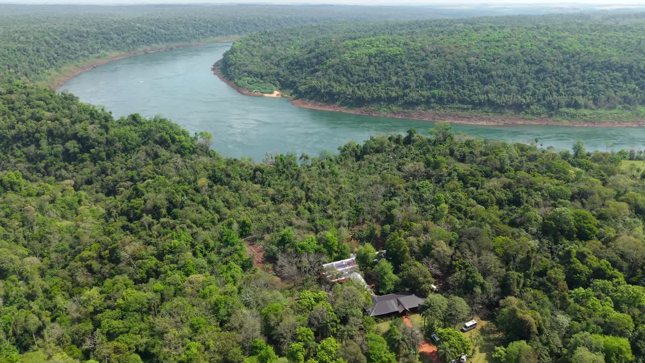 Glamping domes nestled in Misiones jungle near Puerto Iguazú, with Paraná River winding toward Paraguay—where eco-luxury and rainforest biodiversity with cross-border views, aerial establishing shot