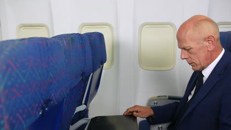 un hombre de negocios maduro abriendo una mesa de bandeja y una computadora portátil en un avión de pasajeros
