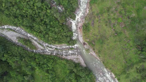 Aerial-orbit-lowering-on-rocky-river-streaming-between-dense-green-woodland-General-Viejo,-Costa-Rica