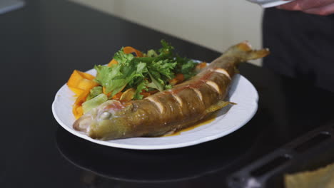 chef preparing and serving roasted trout with vegetables