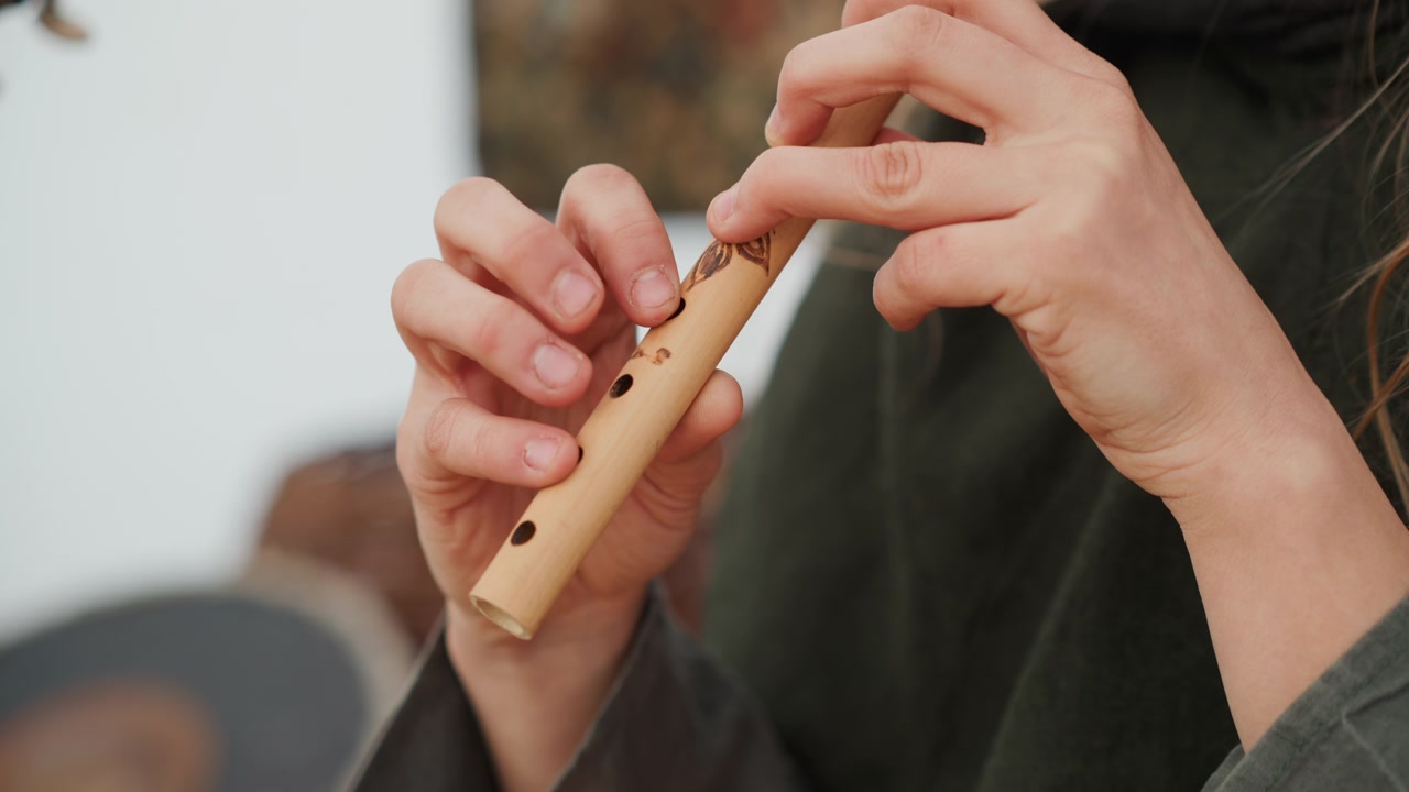 Primo piano delle mani che suonano un piccolo flauto di legno, le dita coprono e sollevano dai fori del tono per modellare la melodia, mentre una leggera sfocatura delle punte delle dita mostra il movimento continuo e una performance guidata dal respiro.