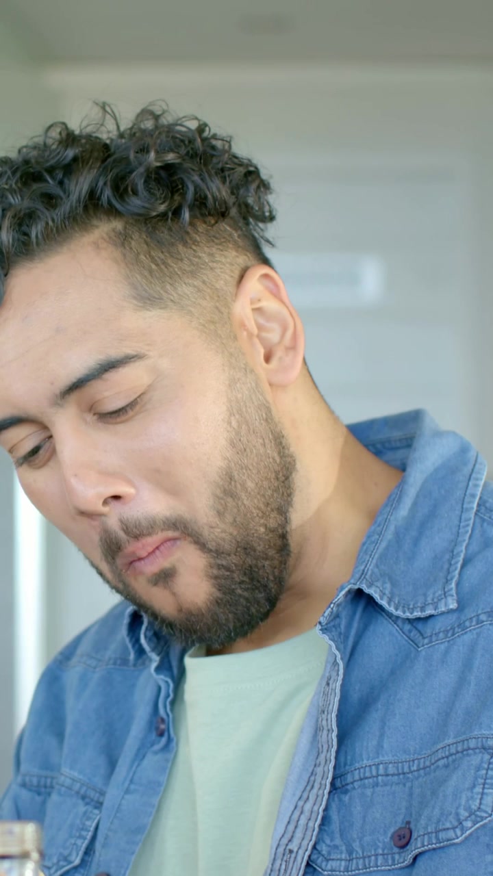 Video verticale: Uomo che annusa un barattolo, assaggia e giudica il sapore al bancone della cucina, indossando una camicia di jeans.