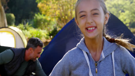 girl smiling at camera while family sitting at tent in background