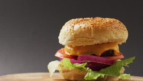 Vídeo-De-Hamburguesa-Con-Queso-Con-Ensalada-En-Pan-De-Hamburguesa,-Sobre-Fondo-Gris-Con-Espacio-Para-Copiar