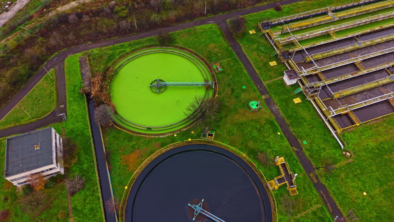 View of a wastewater treatment facility with tanks and machinery located in a green area during daytime