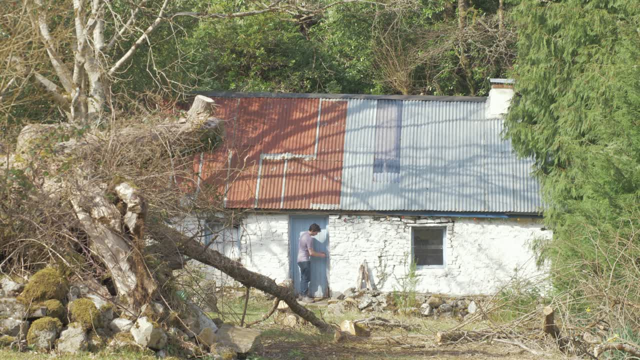 Young man leaving traditional Irish stone cottage in nature