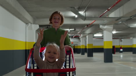 siblings having fun brother pushing sister in shopping cart on supermarket parking lot