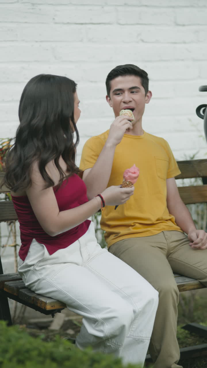 Wide shot of a group of young people sharing and enjoying ice cream on a bench, in a relaxed, outdoor setting.