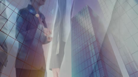 digital composition of mid section of businesspeople shaking hands against tall buildings