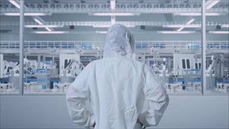 back view of asian male scientist putting hands on his hip and looking around in modern lab factory with automated robots