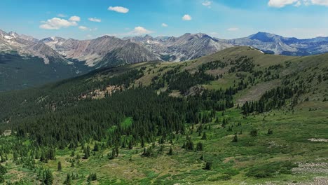 Antena-Sobre-Los-árboles-Y-Colinas-De-Cottonwood-Pass-Con-Las-Montañas-Rocosas-En-El-Fondo,-Colorado,-EE.UU.