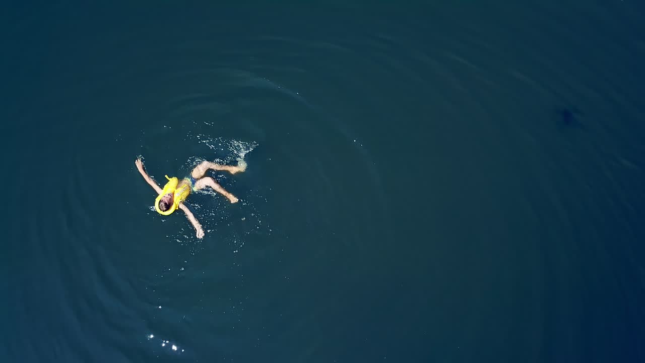 Little boy swimming in crystal clear water. Happy children on summer vacation. Aerial view.