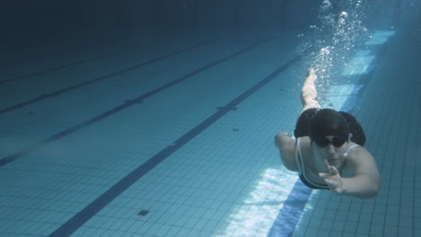 toma submarina de una joven nadadora buceando por el fondo de una piscina