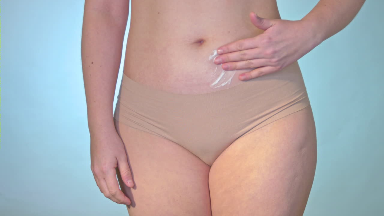 Lubricating the belly with cream. The woman applies a cream or lotion to the skin on her stomach. The woman massages the skin with anti-cellulite cellulite. Skin therapy and care