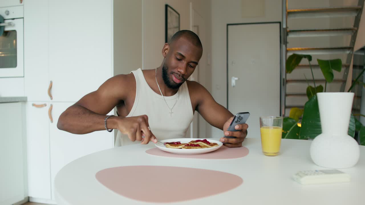 hombre comiendo panqueques y usando teléfono inteligente en la cocina