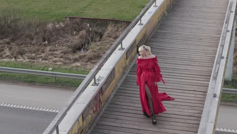 Aerial-drone-shot-of-a-model-in-vibrant-red-dress-flipping-hair-on-a-bridge