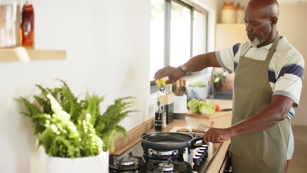 Cooking in kitchen, mature man pouring oil into pan on stove