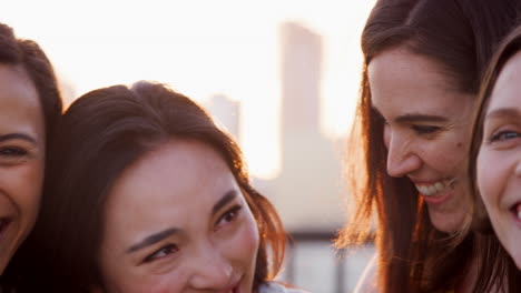 portrait of female friends gathered on rooftop terrace for party with city skyline in background