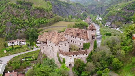 aerial slow glide around castel roncolo (schloss runkelstein) in bolzano, italy, nestled above the talvera river and surrounded by terraced vineyards and alpine slopes