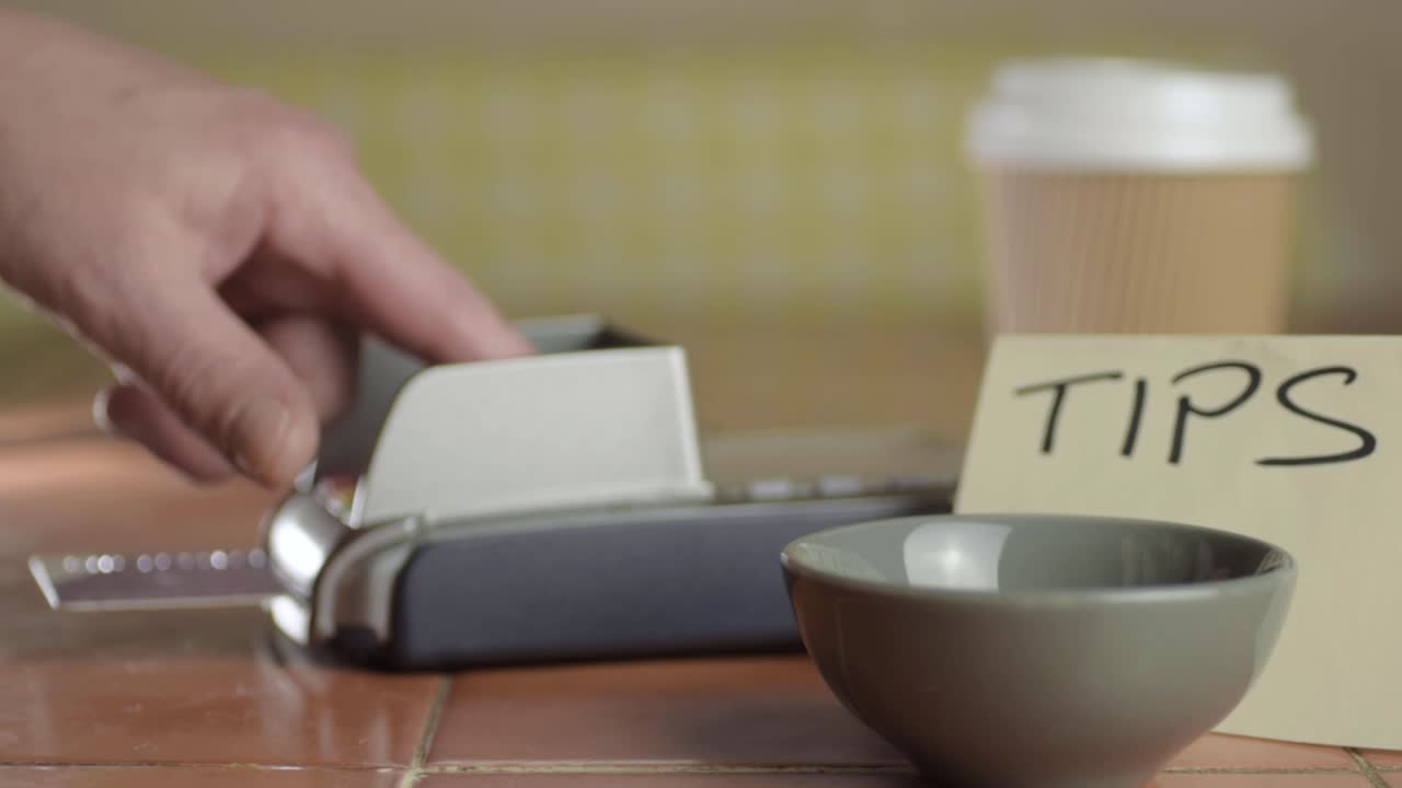 Hand paying by card cafe next to tip box medium shot