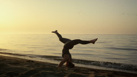 chica delgada manteniendo el equilibrio con la cabeza al aire libre. mujer de yoga entrenando en la playa