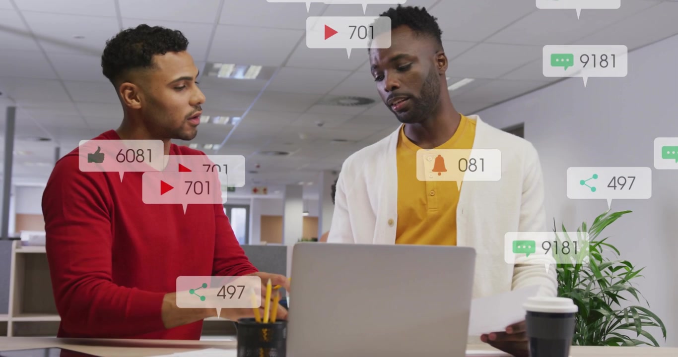 Two coworkers watching laptop as new engagement icons floating over desk, analyzing content metrics