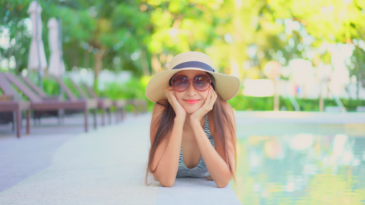 카메라를 바라보는 호텔 수영장 옆에 배를 깔고 누워 있는 아름다운 여성
