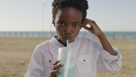 retrato en primer plano de un animado niño afroamericano disfrutando de un batido con auriculares escuchando música bailando juguetón en el parque