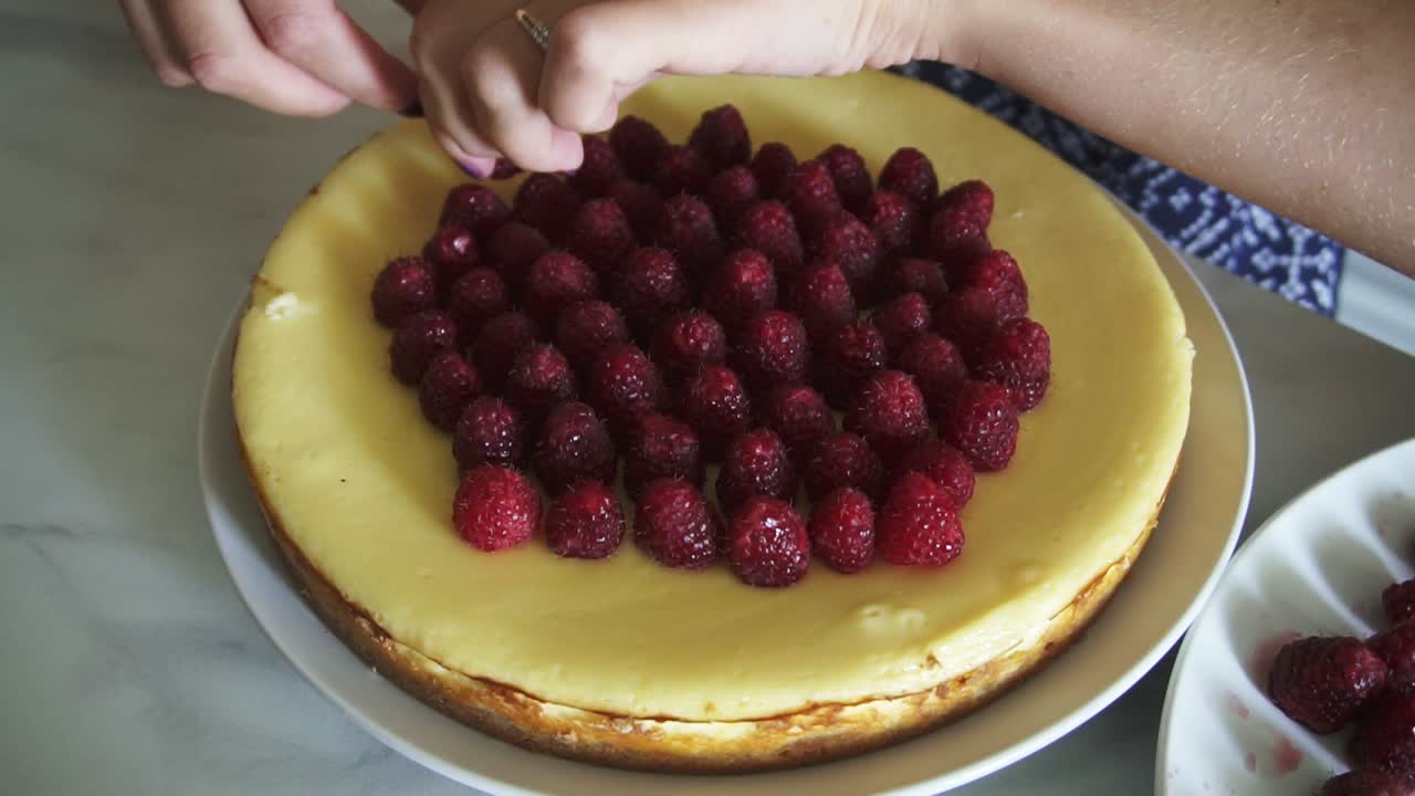 라즈베리로 장식 된 케이크의  ⁇  뷰. 여자는 라즈베리로 케이크의  ⁇ 을 찬양하고 장식하고 있습니다.