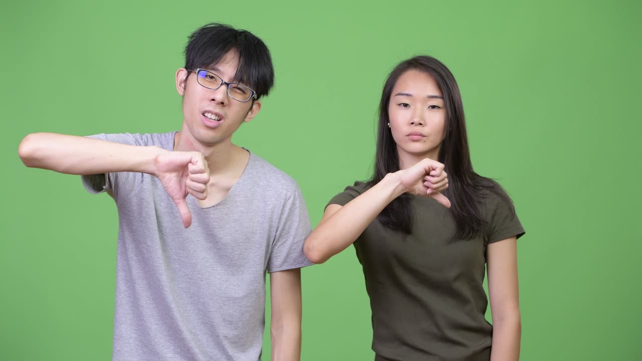 Young Asian couple giving thumbs down together