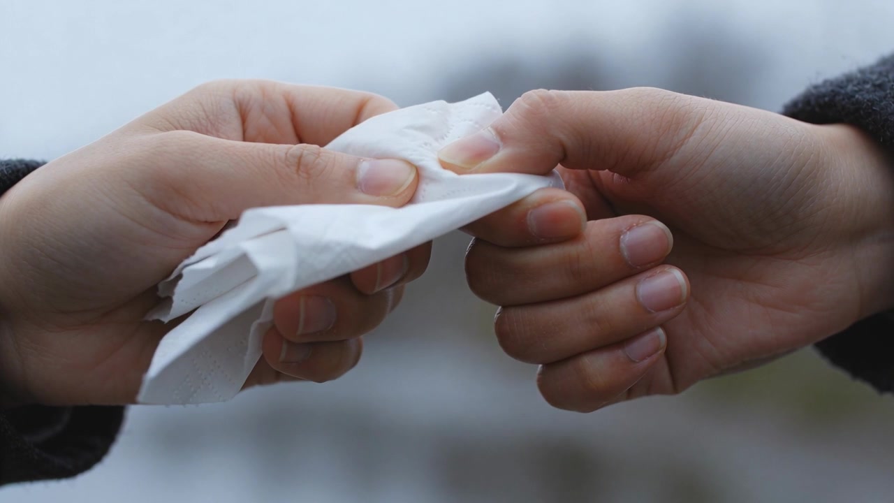 Offering left hand passing crumpled white tissue into right hand at urban street, dark long sleeves